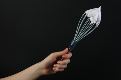 Photo of Woman holding whisk with whipped cream on black background, closeup. Space for text