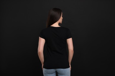 Woman wearing black t-shirt on dark background, back view