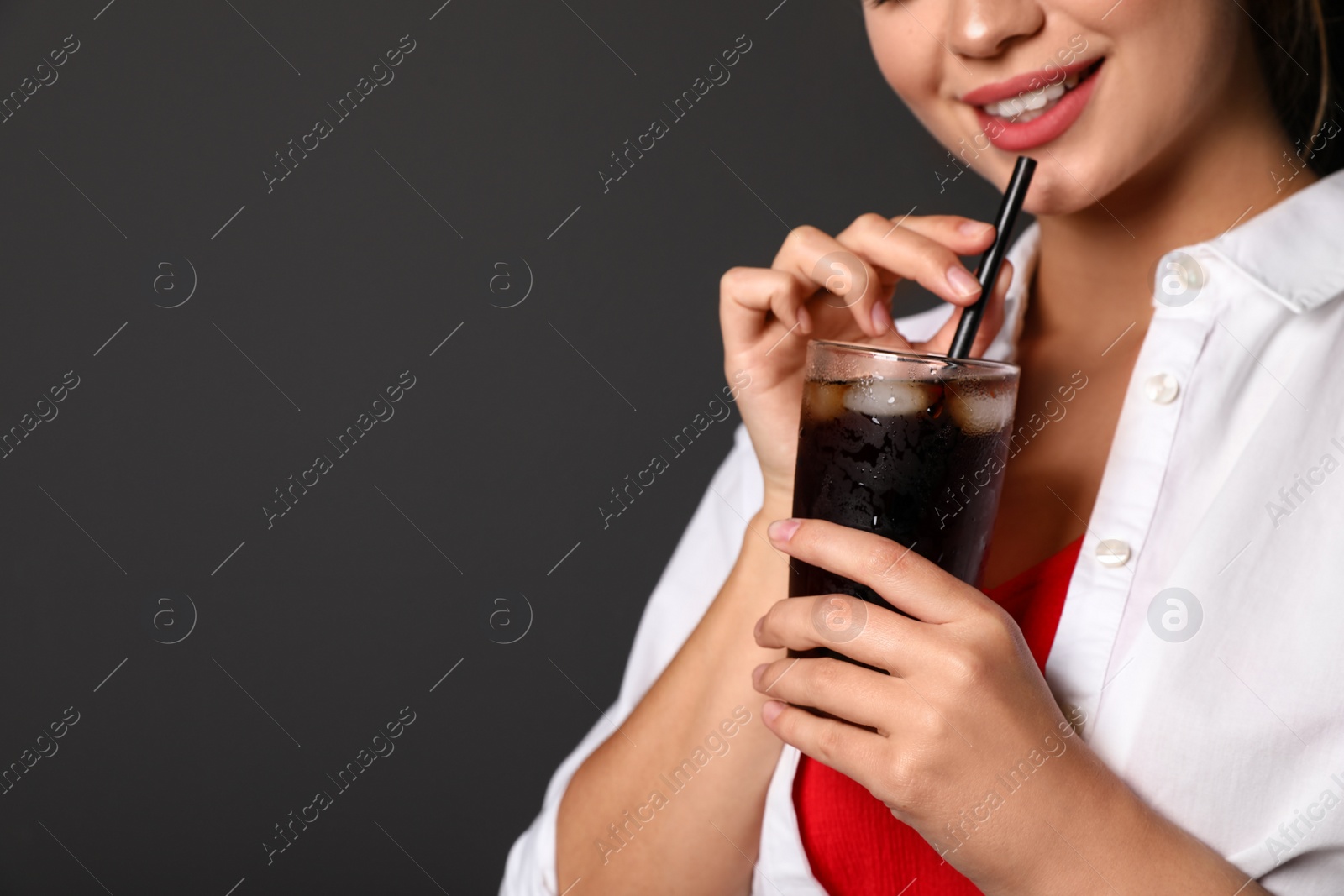 Photo of Young woman holding glass of cola on black background, closeup with space for text. Refreshing drink