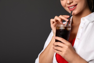 Young woman holding glass of cola on black background, closeup with space for text. Refreshing drink