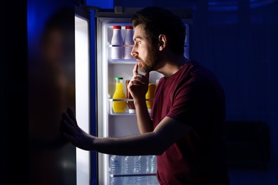 Photo of Man choosing food from refrigerator in kitchen at night. Bad habit