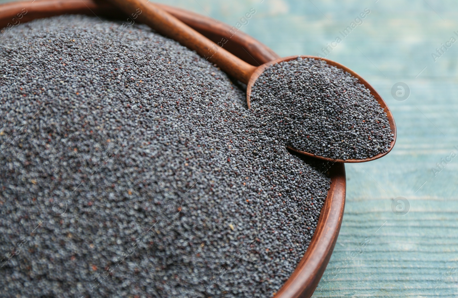 Photo of Poppy seeds in bowl and spoon on blue table, closeup