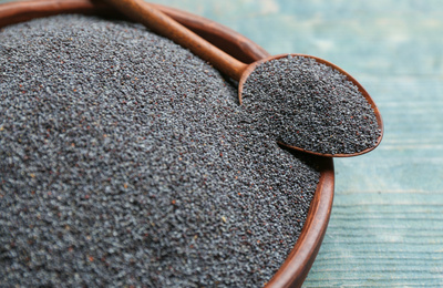 Poppy seeds in bowl and spoon on blue table, closeup