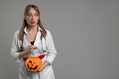 Photo of Woman in scary nurse costume with pumpkin bucket on light grey background, space for text. Halloween celebration