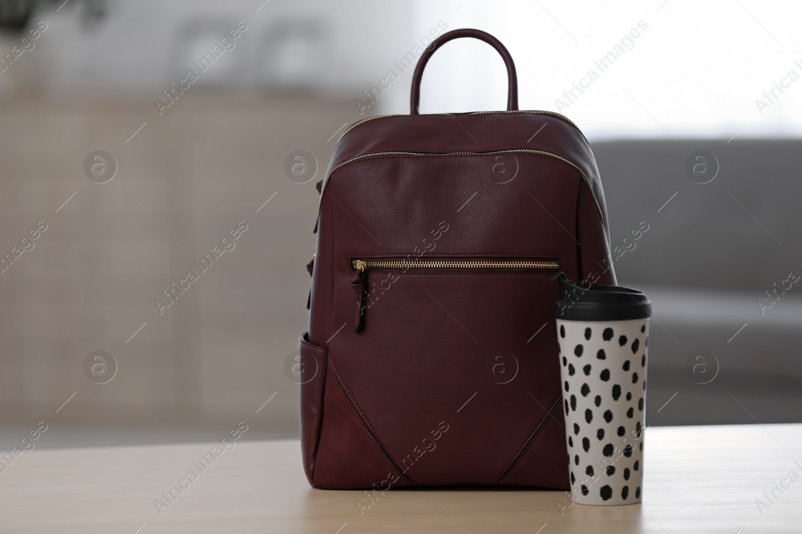 Photo of Stylish burgundy backpack and cup of coffee on wooden table indoors