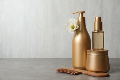 Different hair products, flower and wooden comb on grey table. Space for text