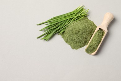 Photo of Pile of wheat grass powder, scoop and fresh sprouts on light grey table, flat lay. Space for text