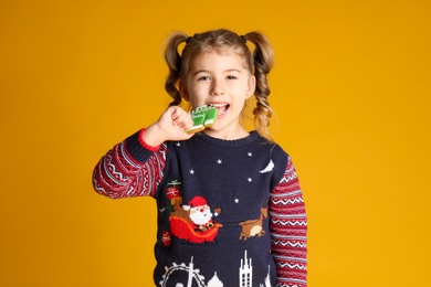 Photo of Cute little girl with Christmas gingerbread cookie on yellow background