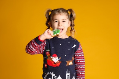 Cute little girl with Christmas gingerbread cookie on yellow background