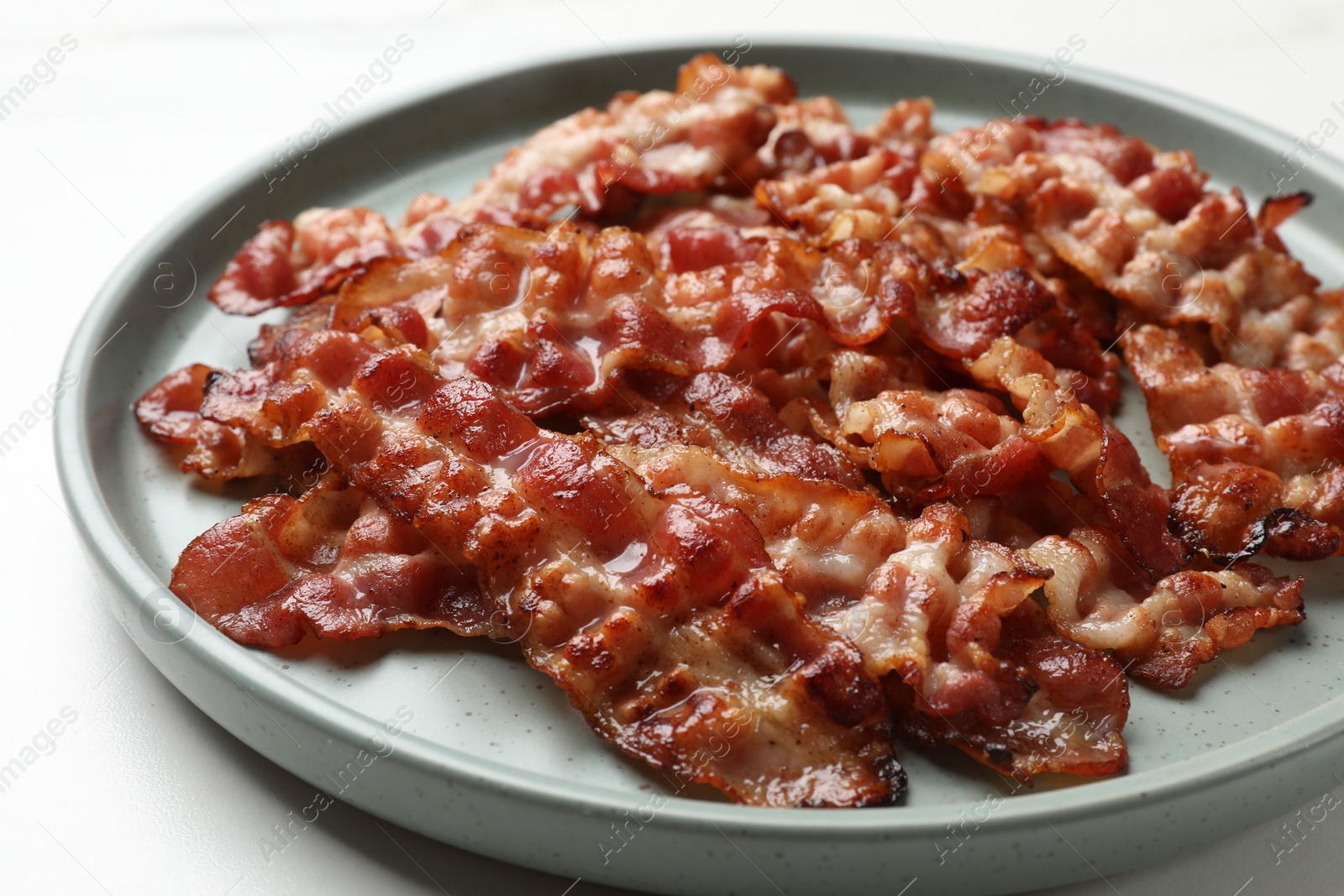 Photo of Slices of tasty fried bacon on white table, closeup