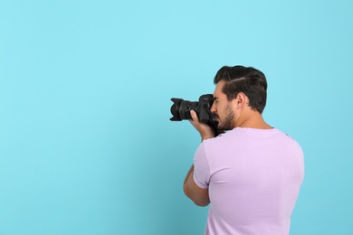 Photo of Young professional photographer taking picture on light blue background. Space for text
