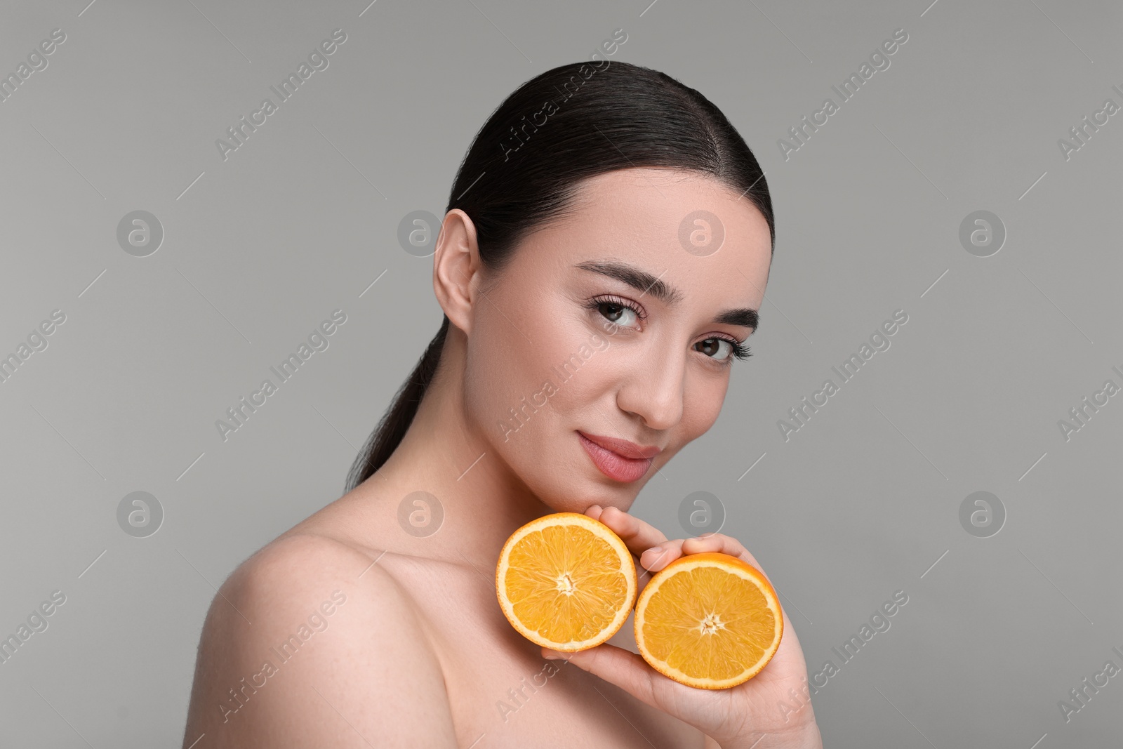 Photo of Beautiful young woman with pieces of orange on grey background