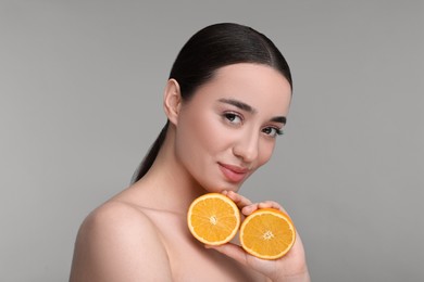 Beautiful young woman with pieces of orange on grey background