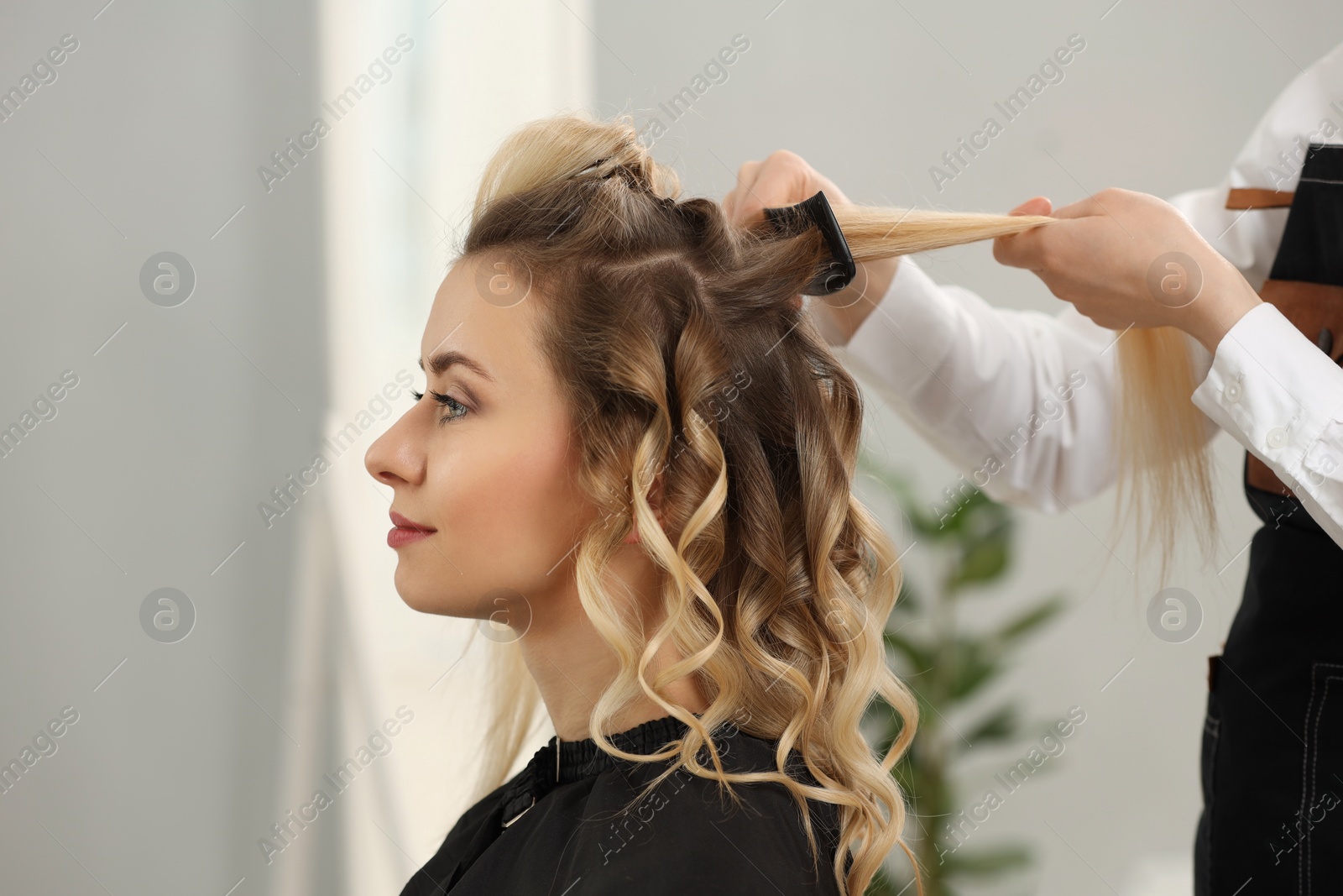 Photo of Hair styling. Professional hairdresser combing woman's hair in salon, closeup