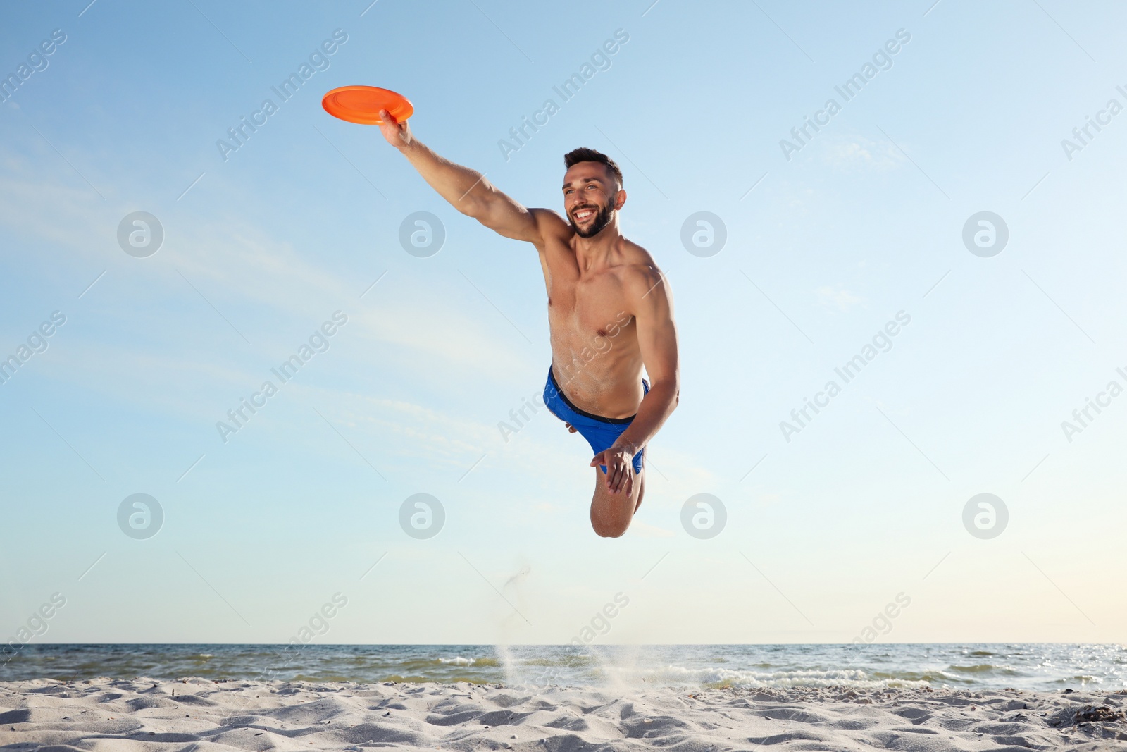 Photo of Sportive man jumping and catching flying disk at beach