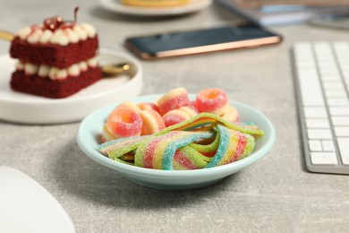 Photo of Bad eating habits at workplace. Bowl with candies on light grey table, closeup