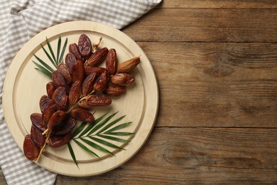 Photo of Sweet dried dates with green leaves on wooden table, flat lay. Space for text