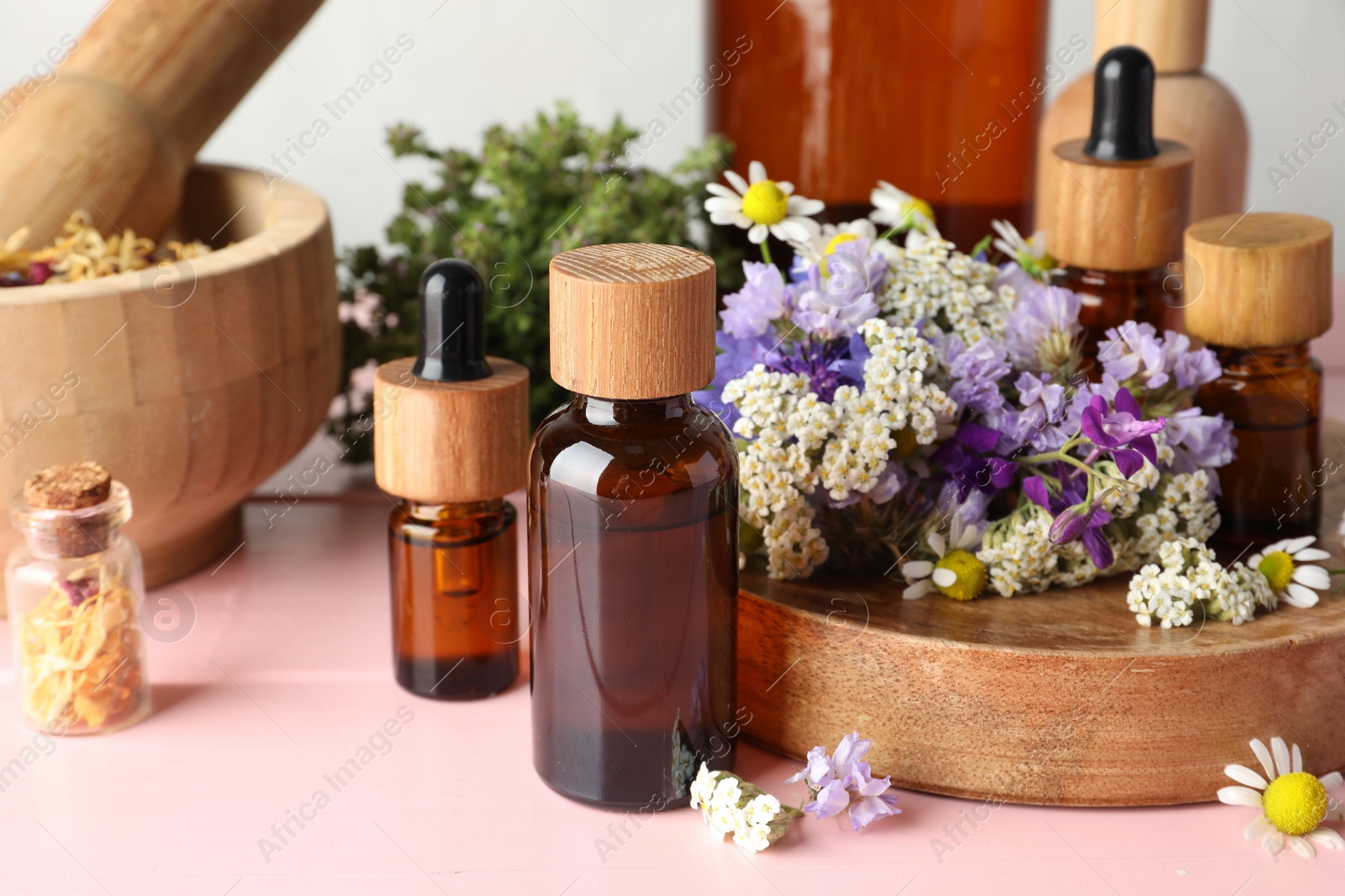 Photo of Aromatherapy. Different essential oils, mortar, pestle and flowers on pink wooden table