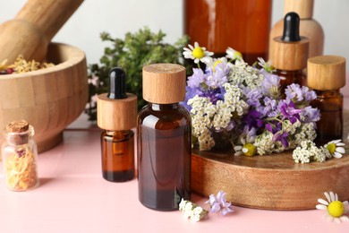 Aromatherapy. Different essential oils, mortar, pestle and flowers on pink wooden table