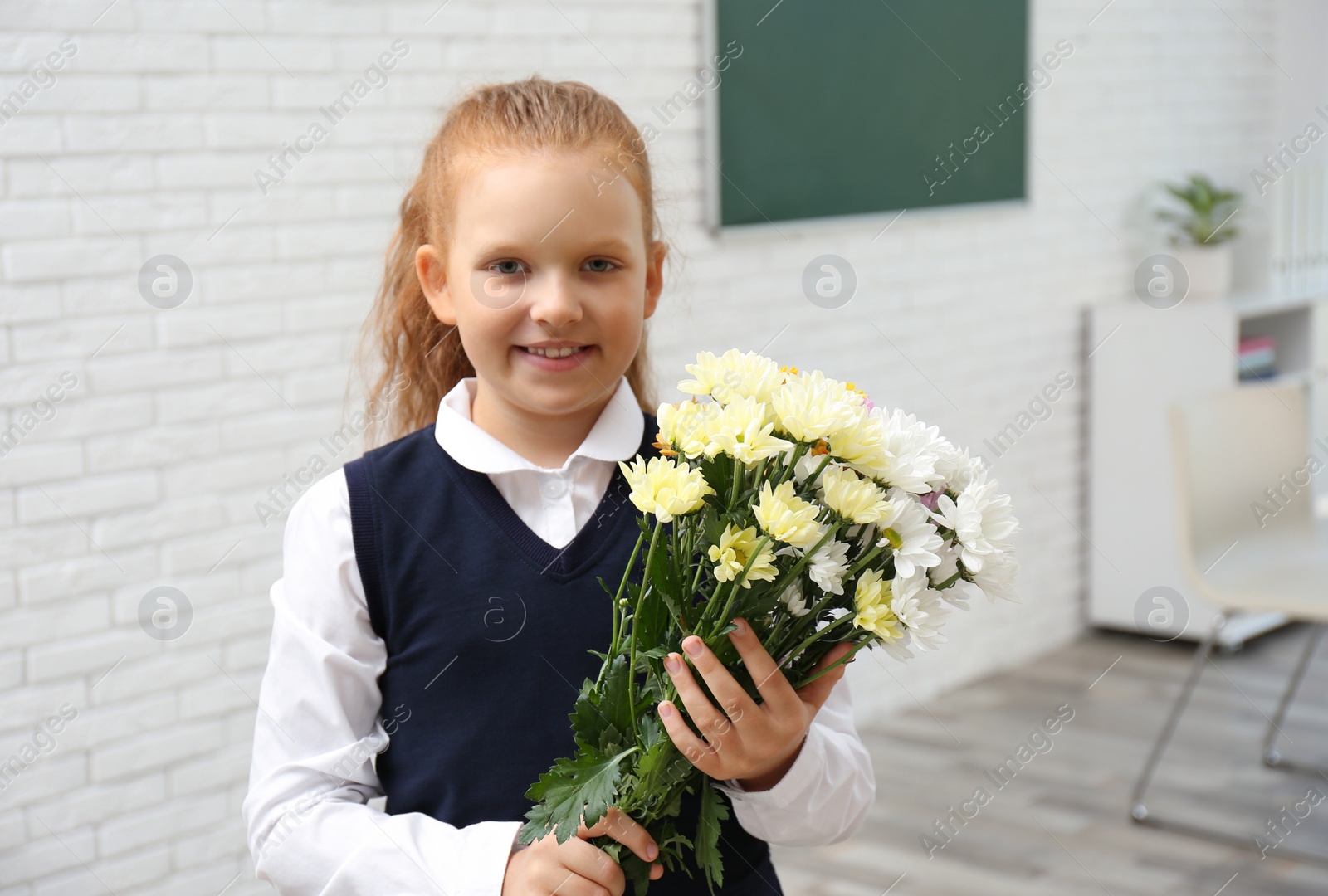 Photo of Happy schoolgirl with bouquet in classroom. Teacher's day