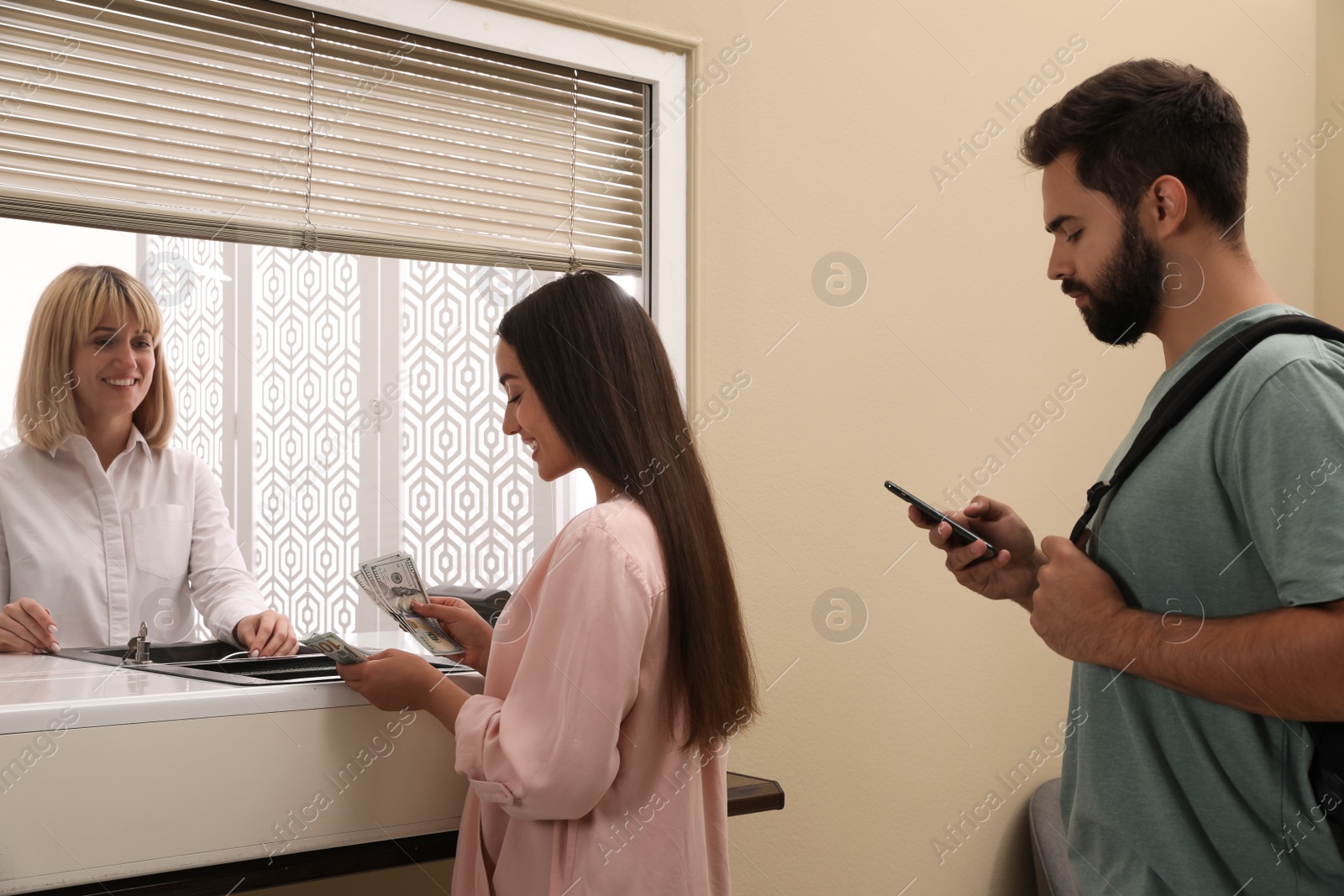 Photo of Young woman with money at cash department window in bank. Currency exchange