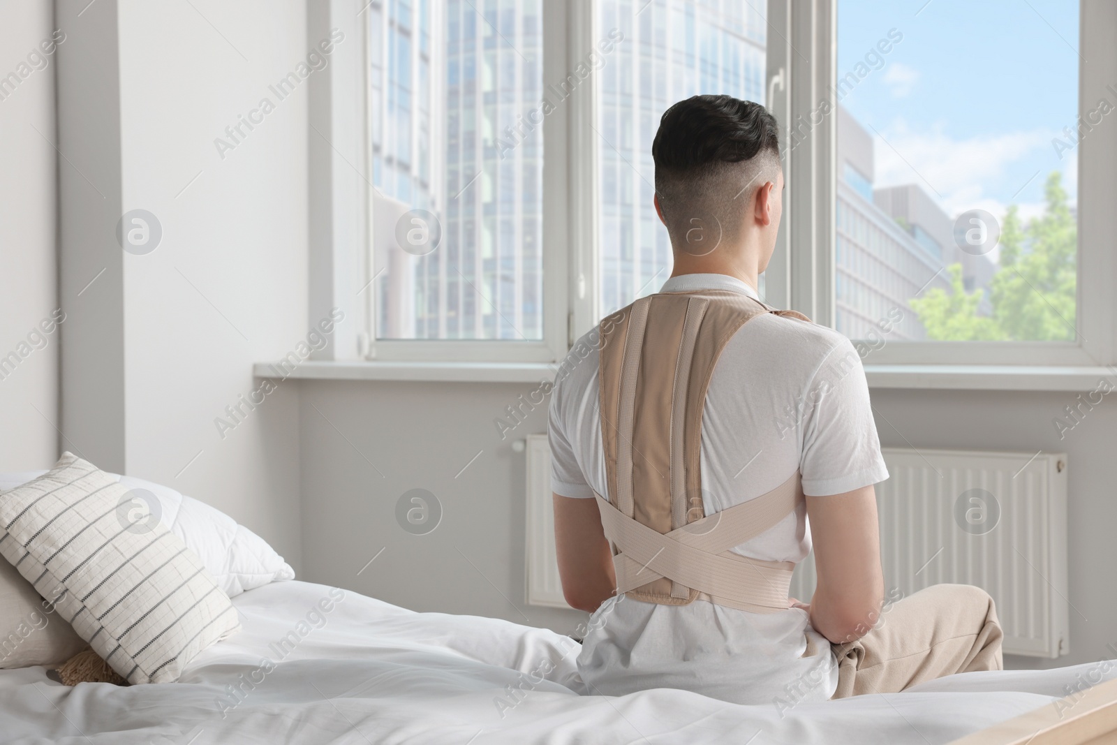 Photo of Man with orthopedic corset sitting in bedroom, back view
