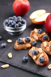 Photo of Fresh apples with peanut butter and blueberries on dark table, closeup