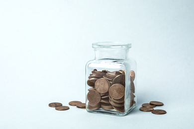 Glass jar with coins on light background