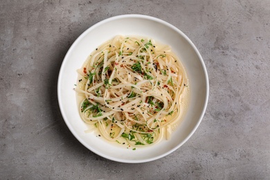 Photo of Plate of noodles with broth and herb on grey background, top view