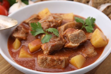 Delicious goulash in bowl on wooden board, closeup