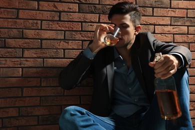 Photo of Addicted man drinking alcohol near red brick wall