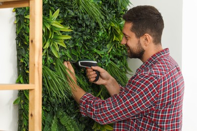 Man with screwdriver installing green artificial plant panel on white wall in room