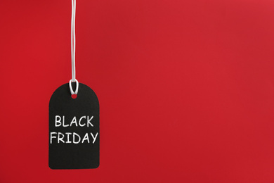 Blank tag hanging on red background, space for text. Black Friday concept