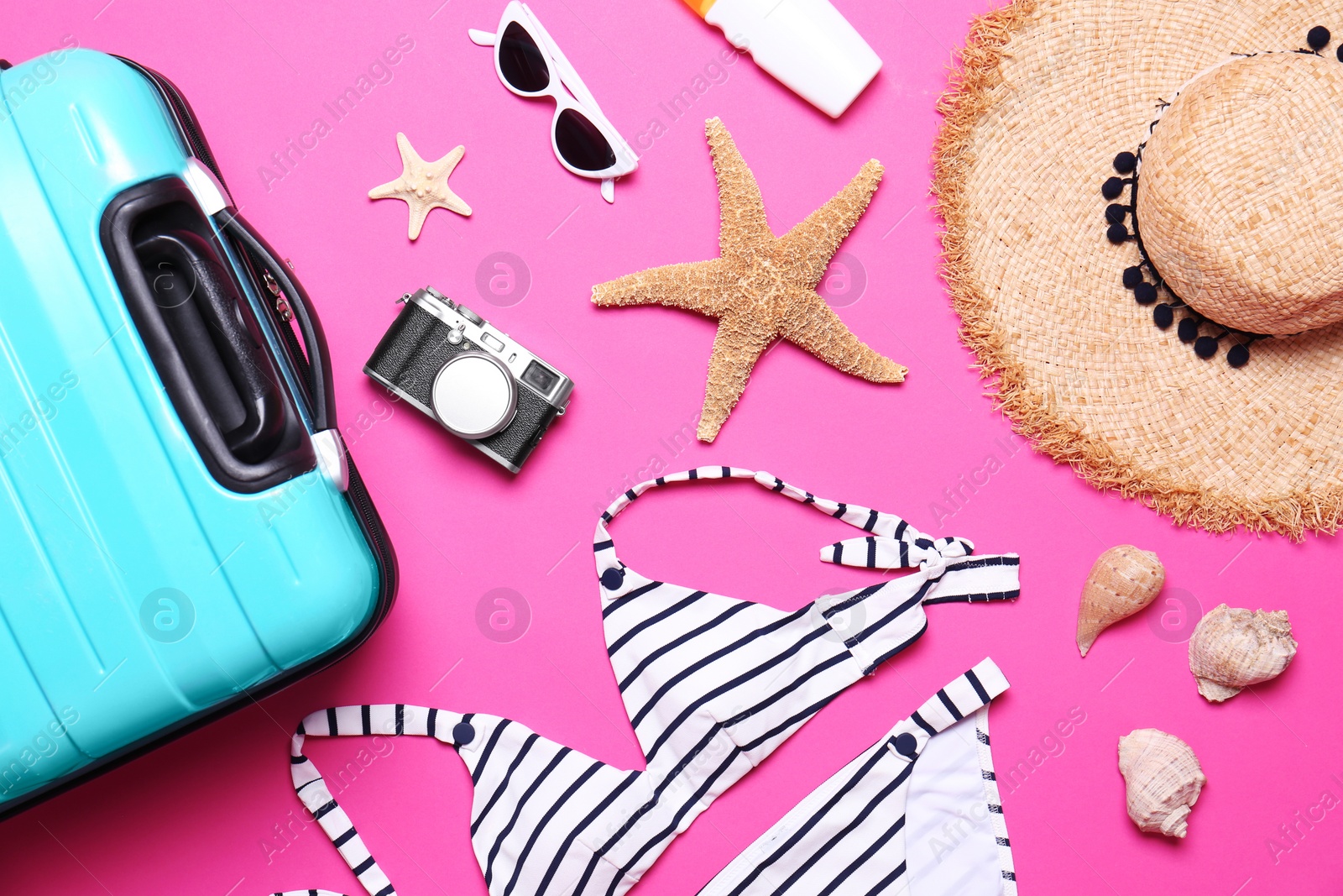 Photo of Flat lay composition with suitcase and beach objects on pink background