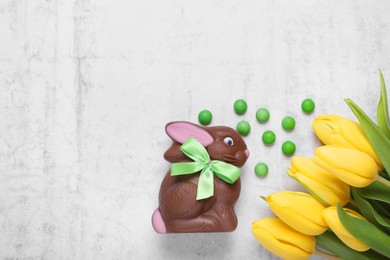 Photo of Flat lay composition with chocolate Easter bunny, beautiful tulips and candies on white textured table. Space for text