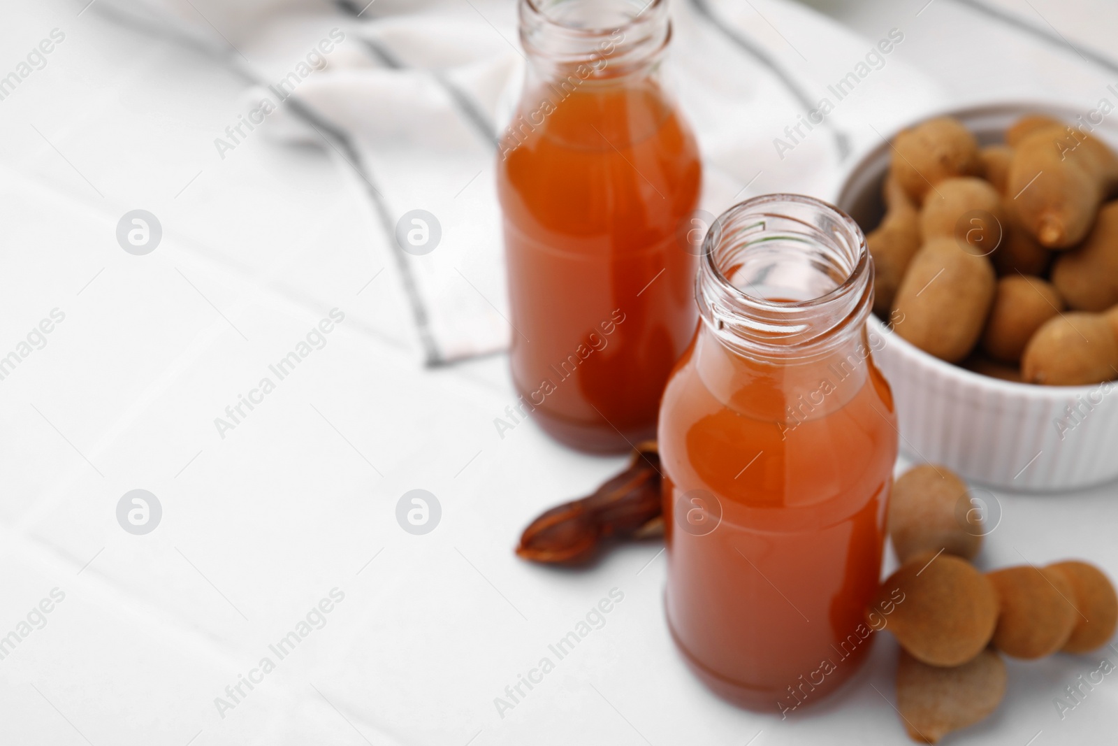 Photo of Tamarind juice and fresh fruits on white tiled table, space for text