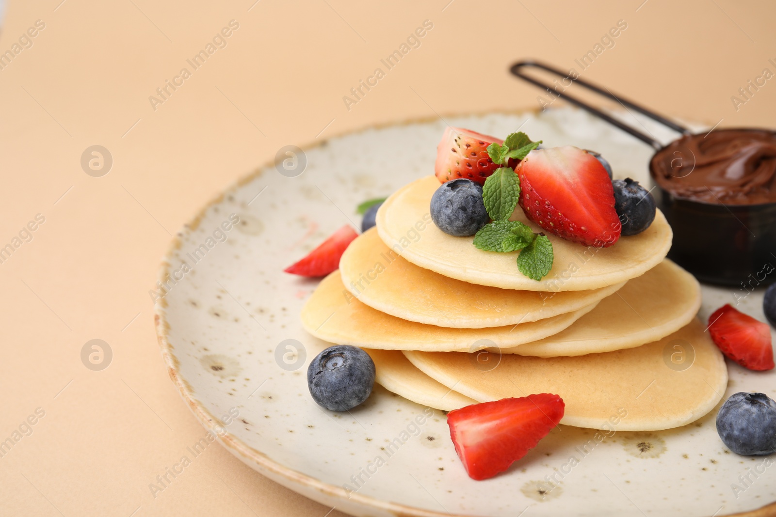 Photo of Delicious pancakes served with berries and chocolate spread on beige background, closeup. Space for text