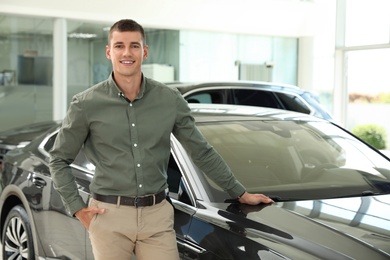 Photo of Young man near new car in modern auto dealership. Space for text