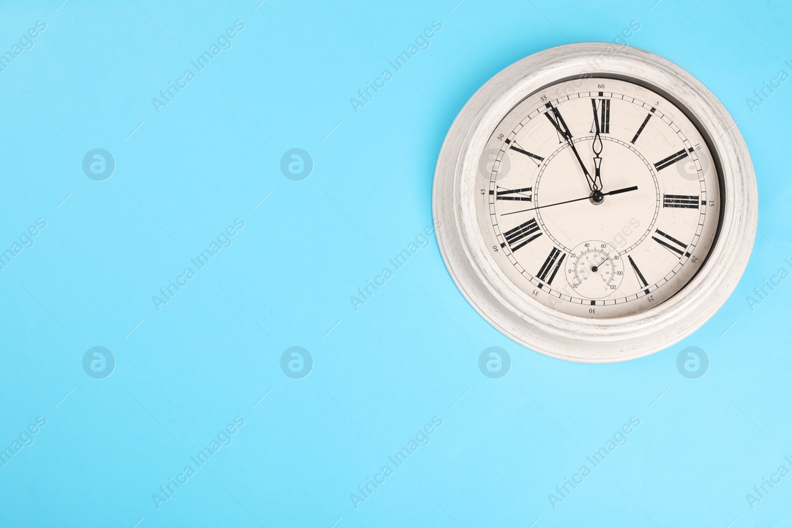 Photo of Stylish vintage wall clock showing five minutes until midnight on turquoise background, top view with space for text. New Year countdown