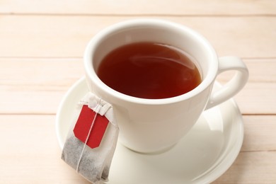 Photo of Tea bag and cup of hot beverage on light wooden table, closeup