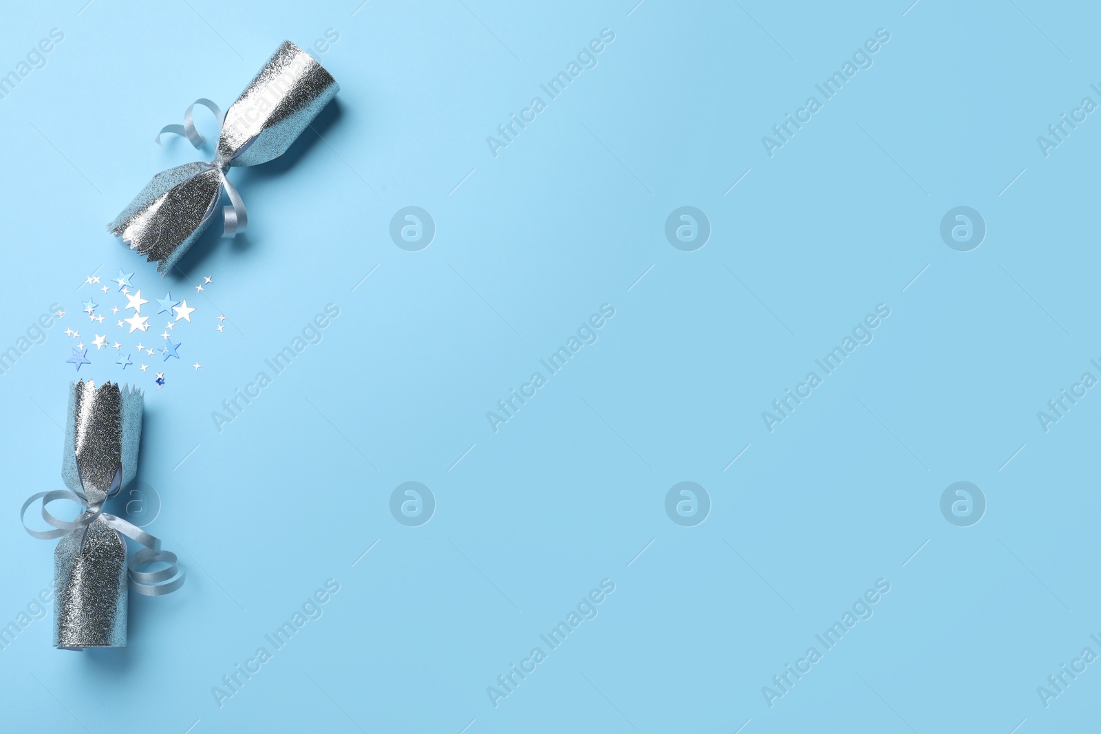 Photo of Open silver Christmas cracker with shiny confetti on light blue background, top view. Space for text
