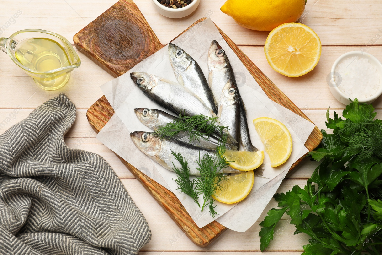 Photo of Fresh raw sprats, lemon and dill on light wooden table, flat lay