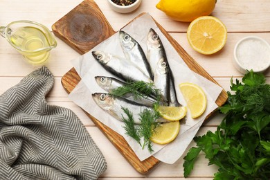 Photo of Fresh raw sprats, lemon and dill on light wooden table, flat lay