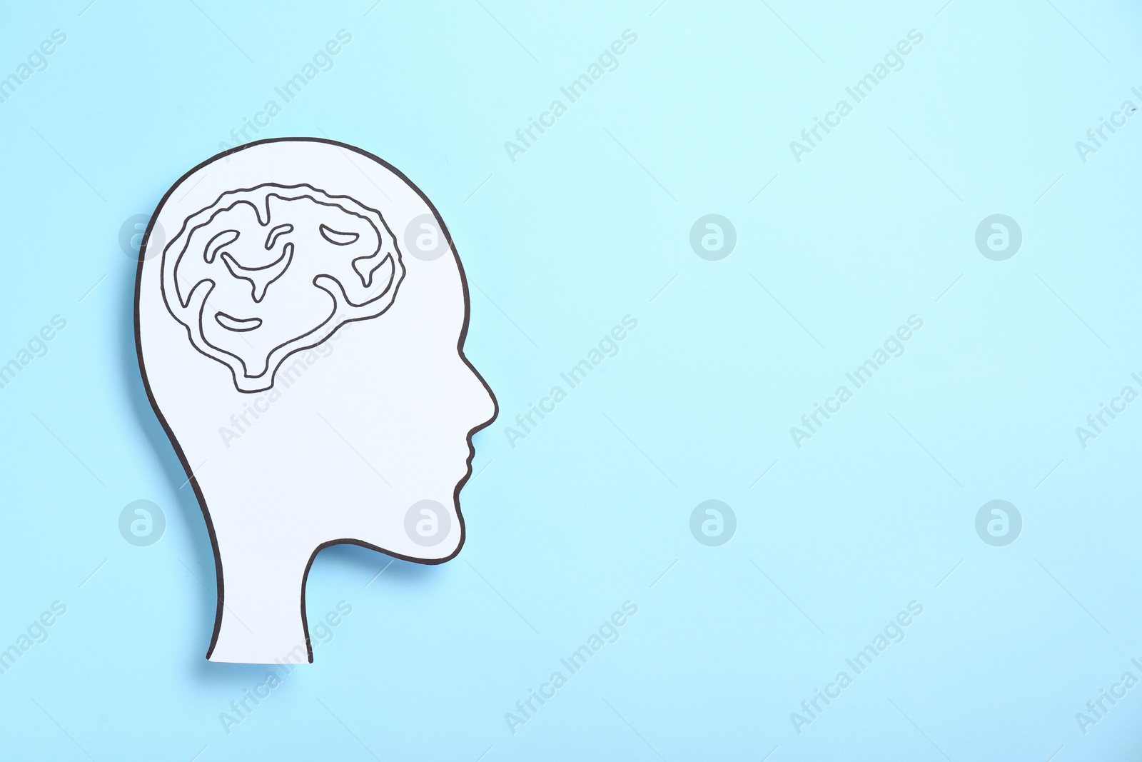 Photo of Paper human head cutout with drawing of brain on light blue background, top view. Space for text