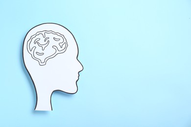 Photo of Paper human head cutout with drawing of brain on light blue background, top view. Space for text