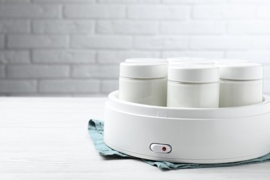 Photo of Modern yogurt maker with full jars on white wooden table. Space for text