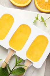 Photo of Tasty orange ice pops in mold on light grey table, flat lay. Fruit popsicle