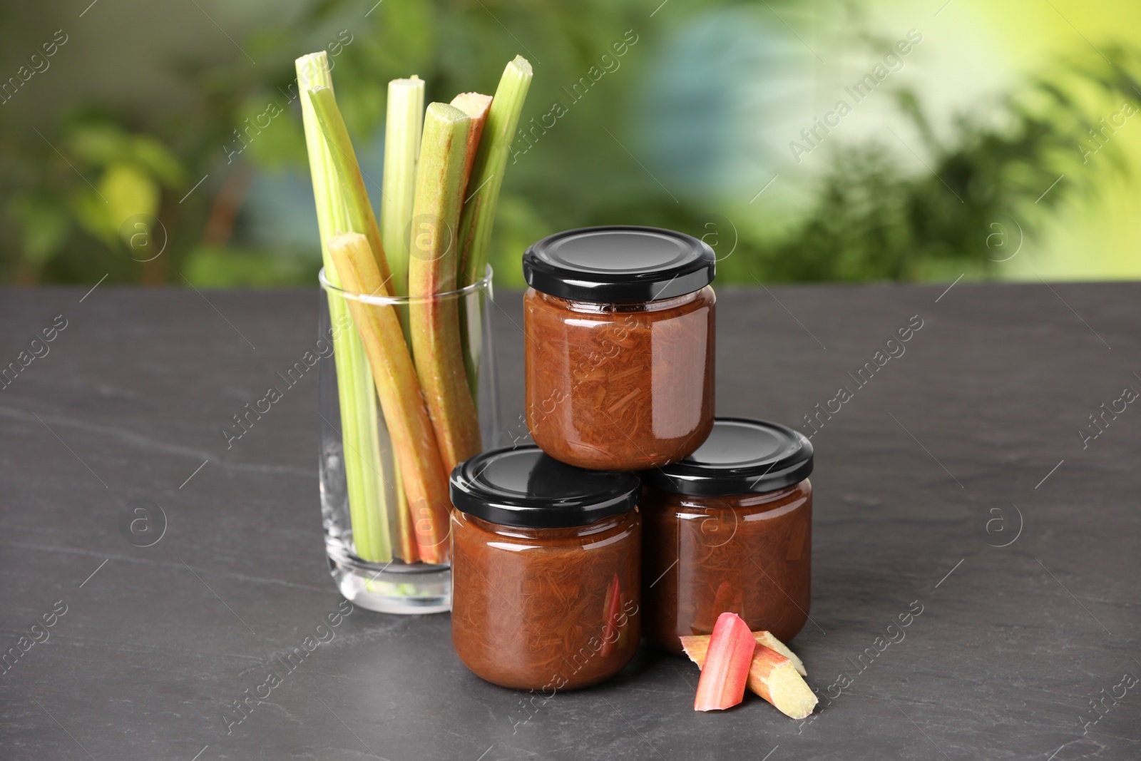 Photo of Jars of tasty rhubarb jam and stalks on grey table