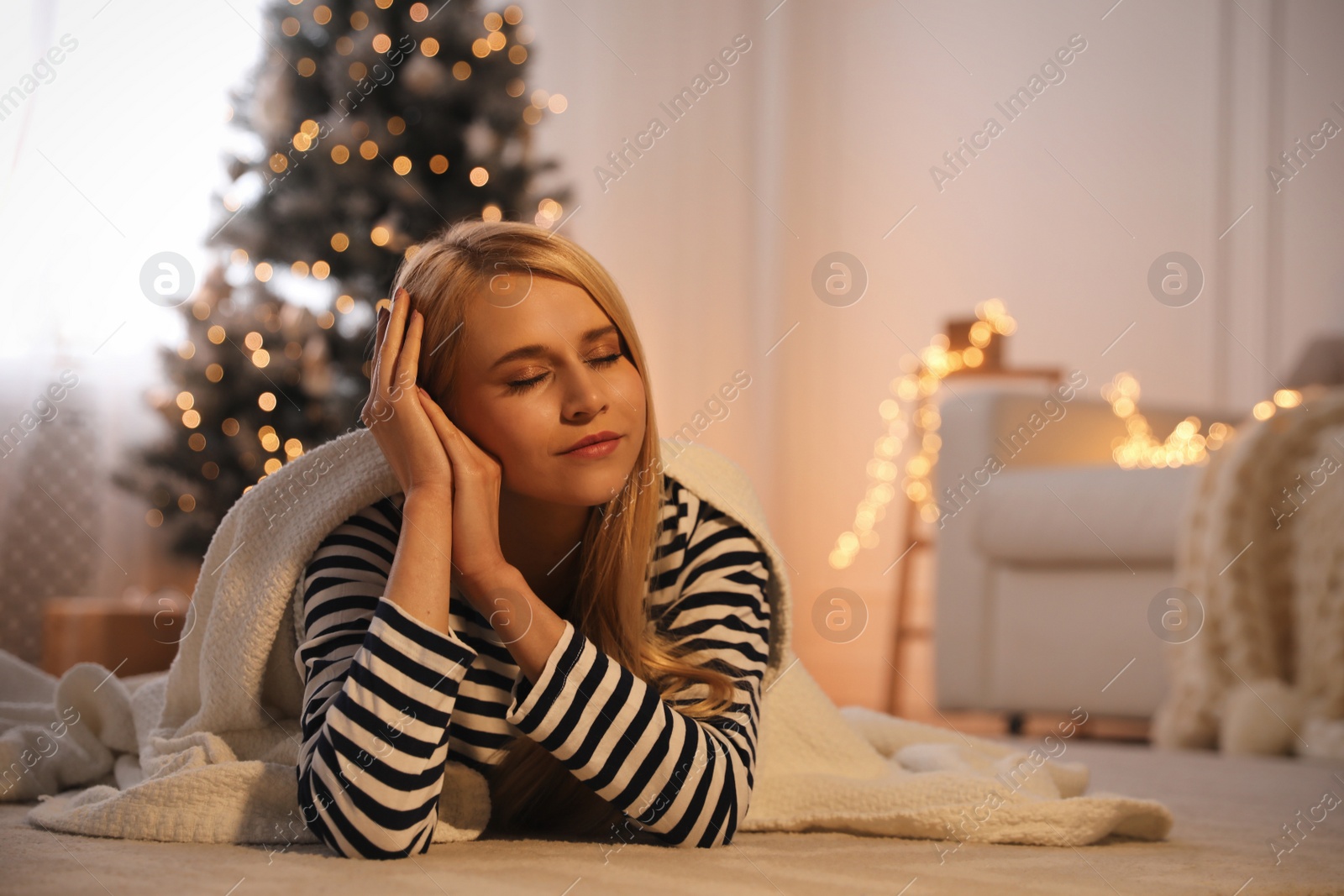 Photo of Young woman with blanket on carpet at home, space for text. Christmas celebration
