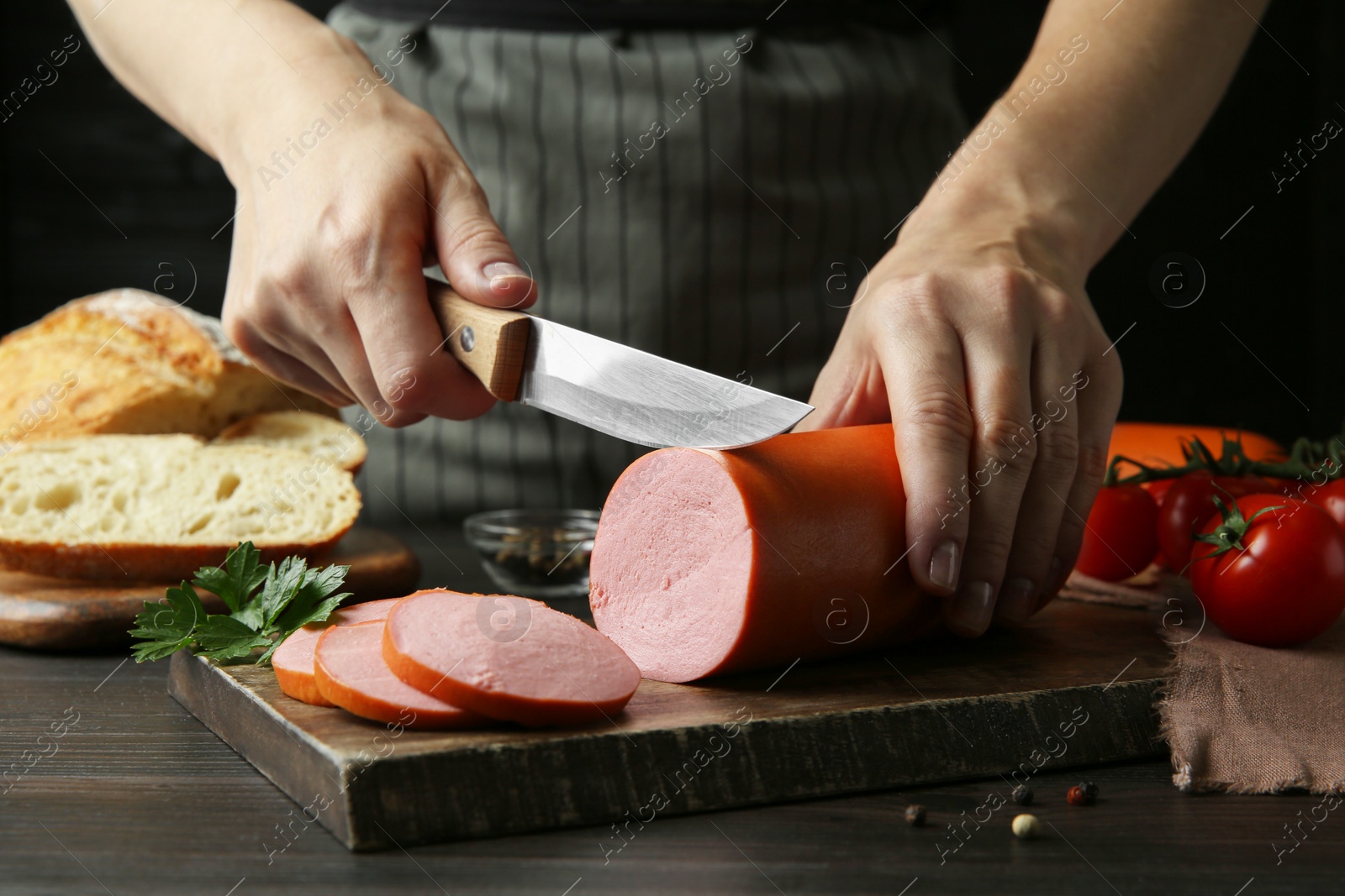 Photo of Woman cutting tasty boiled sausage at dark wooden table, closeup